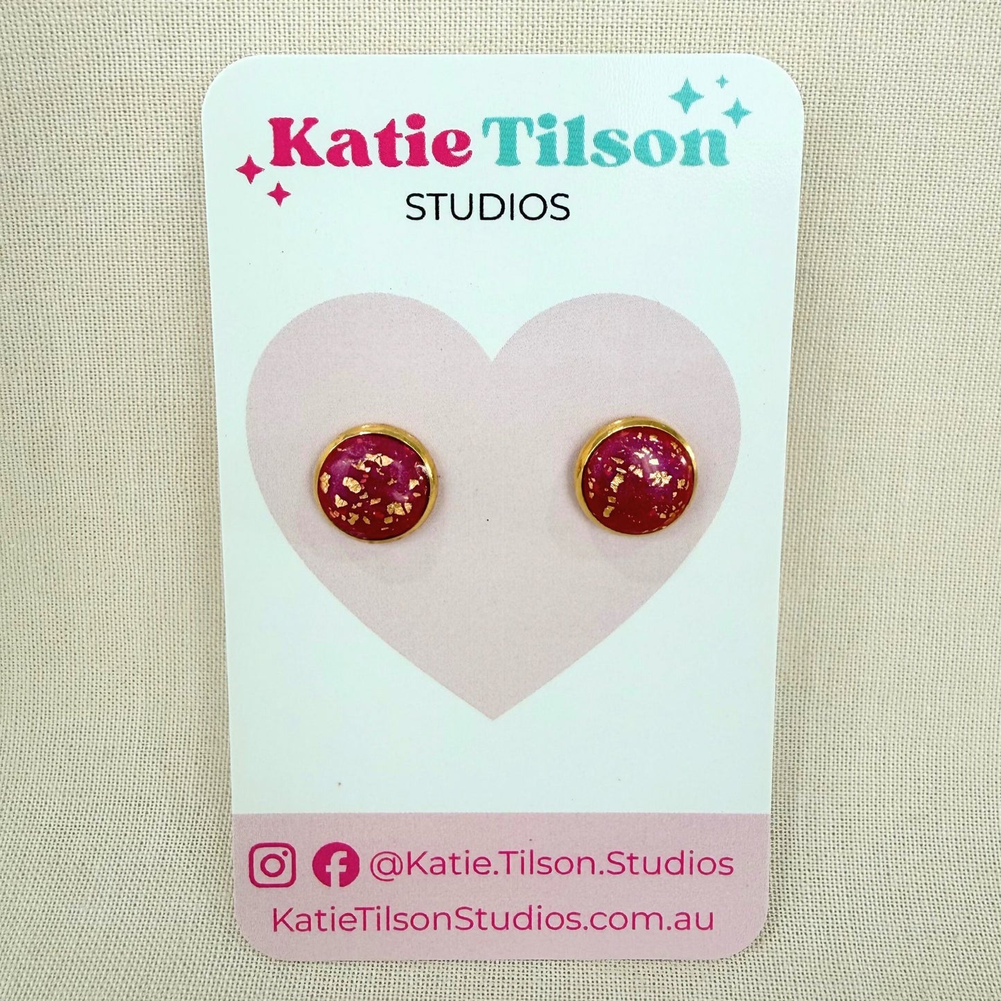 Magenta and gold earrings stud on a Katie Tilson Studios card against a beige background.