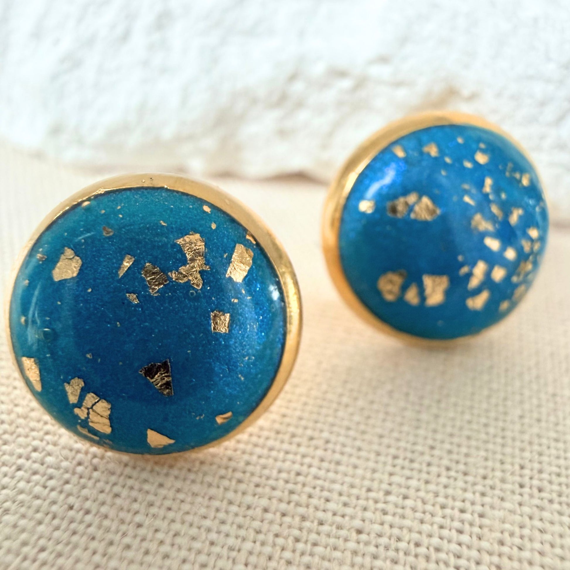 Close up of Good Vibes handmade stud earrings in teal colour with gold flecks and gold bezel.