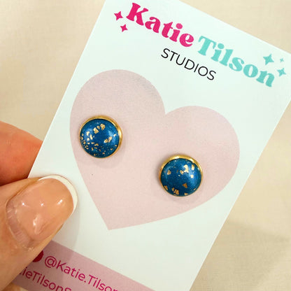 Teal stud earrings with gold accents on a Katie Tilson Studios card held by a hand.