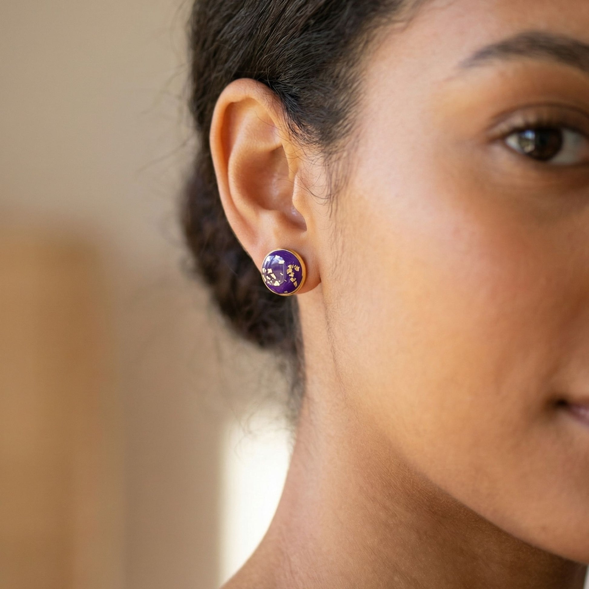 Close-up of a woman wearing a purple stud earring with gold accents.