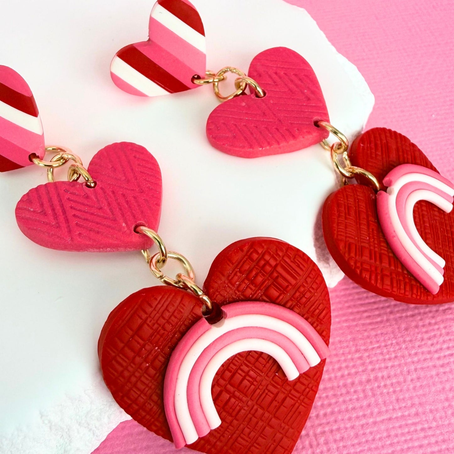 Close up of Australian handmade statement earrings in a polymer clay heart design with rainbow detail and gold hardware.