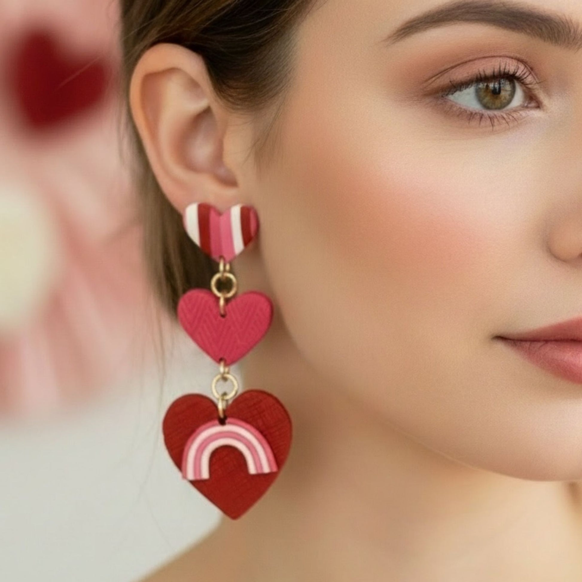 Close-up of a woman wearing heart-shaped statement earrings with a heart and rainbow design.