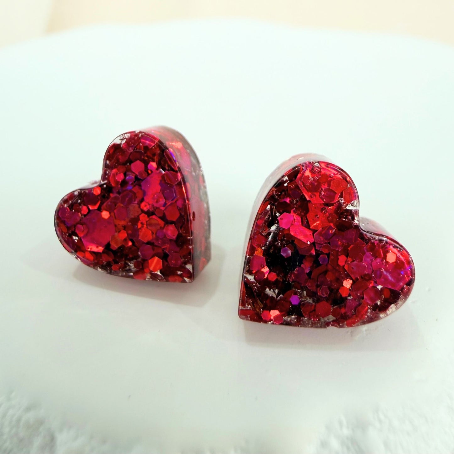 Pink resin glittery heart-shaped stud earrings on a white background.