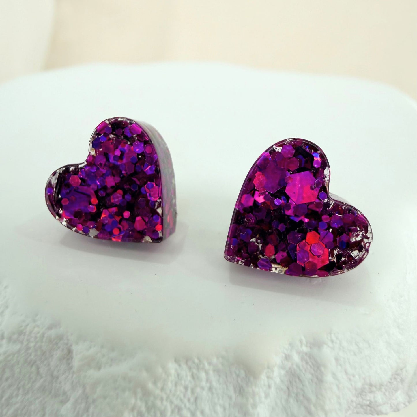Purple heart-shaped resin glitter stud earrings on a white surface.
