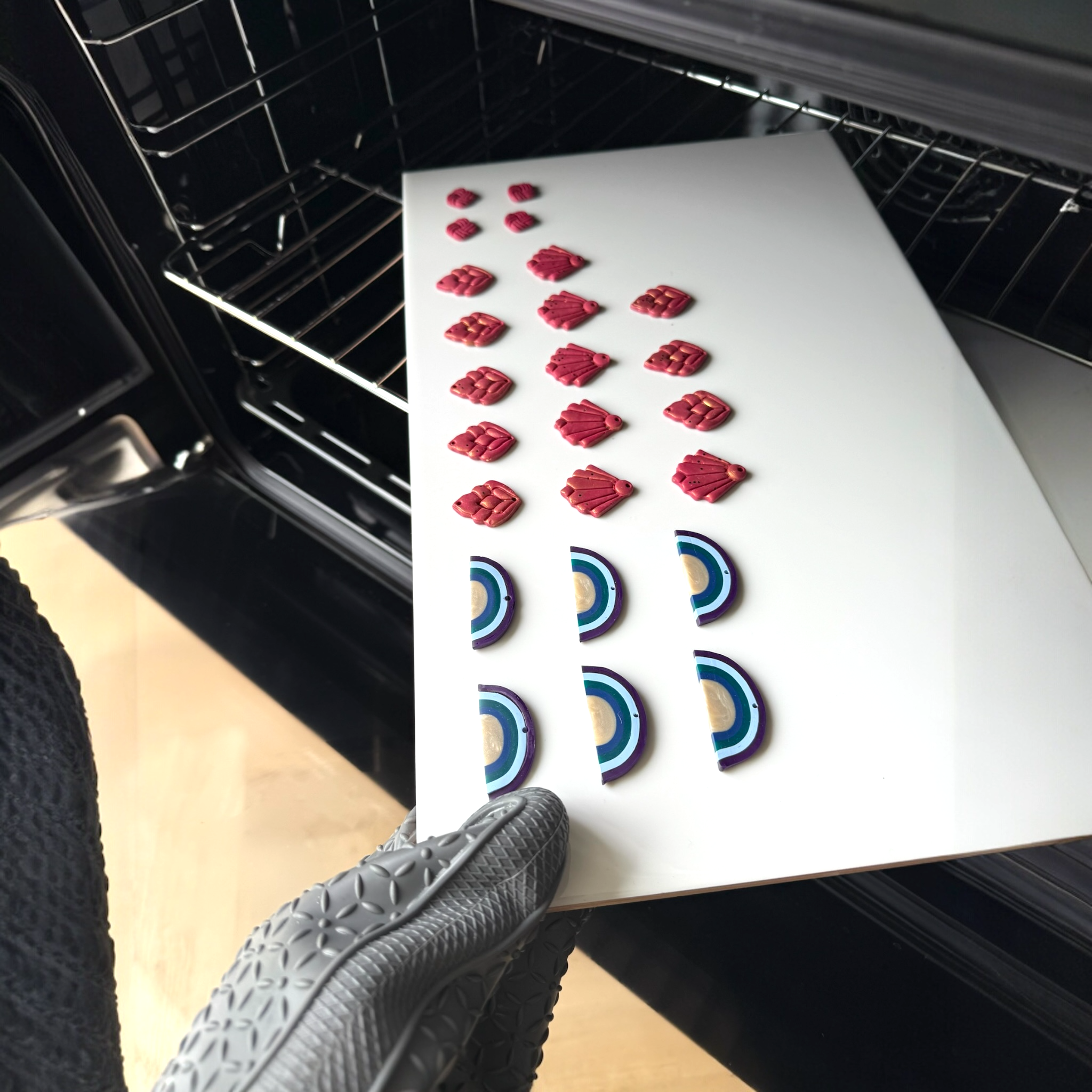 Hand holding red and blue polymer clay earrings designs coming out of an open oven after baking.