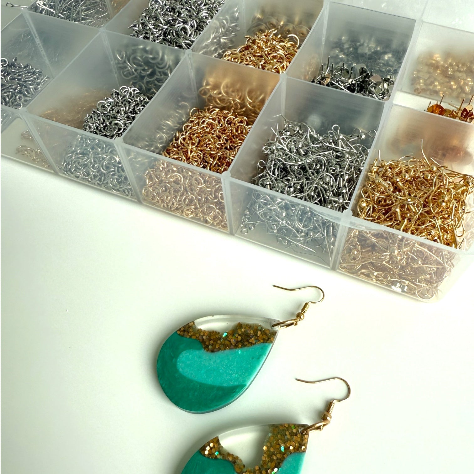 Metal jewellery-making findings in a clear organizer with a completed set of handmade resin earrings.