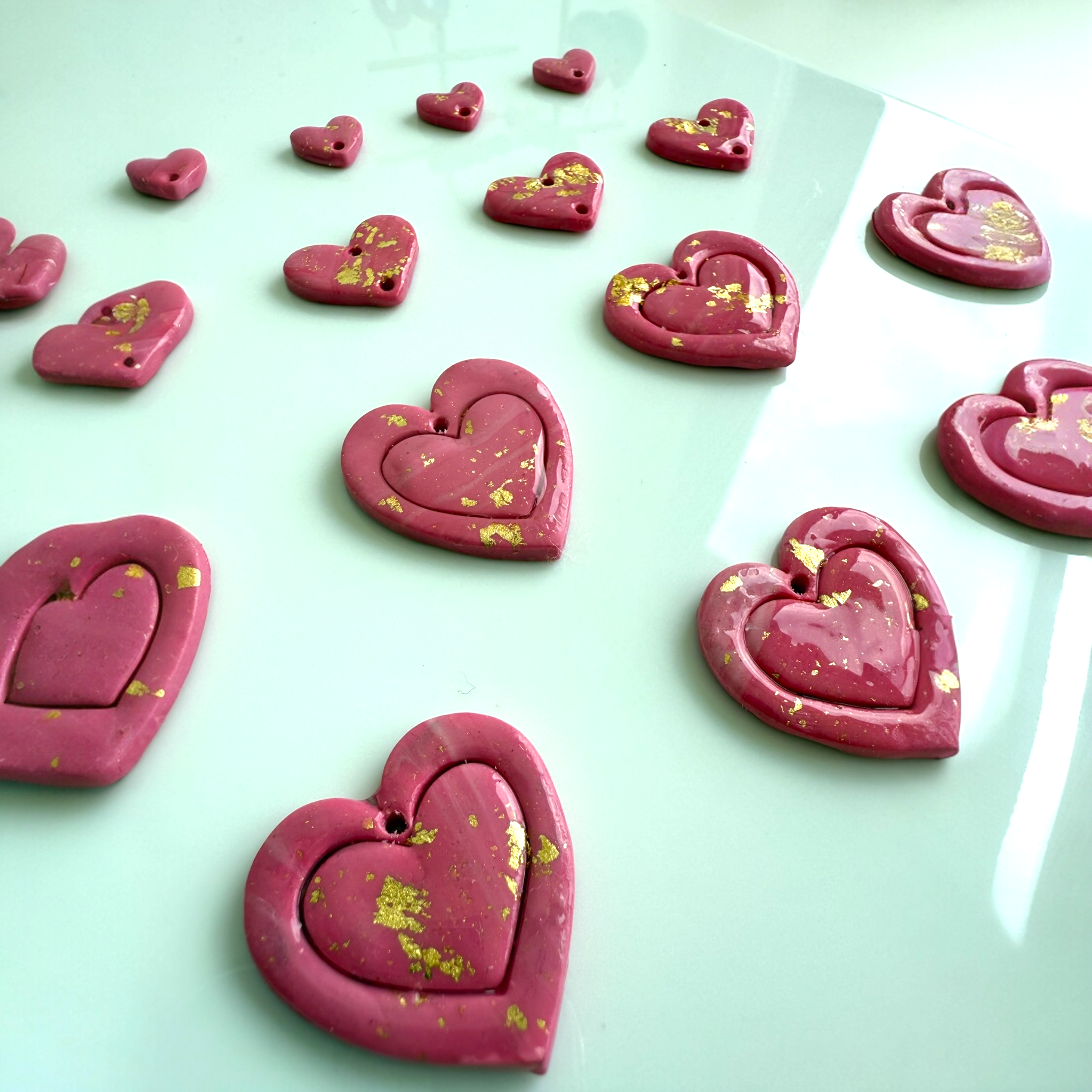 Pink heart-shaped polymer clay earrings with gold specks on a light green glass surface