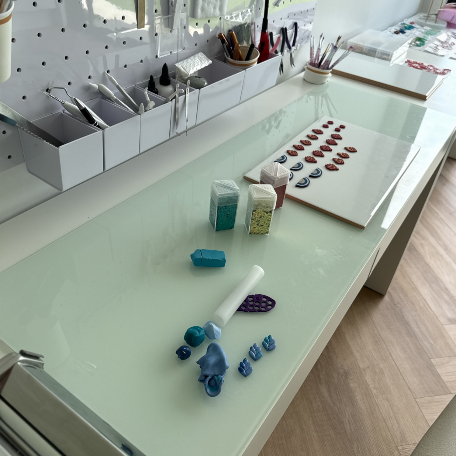 White glass countertop with blocks of polymer clay, glitters and clay tools.