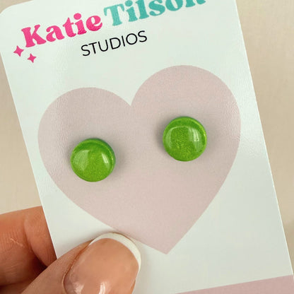 Lime green round stud earrings on a Katie Tilson Studios card held by a hand.