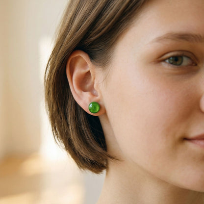 Close-up of a woman wearing lime green stud earrings with a glossy finish against blurred background.