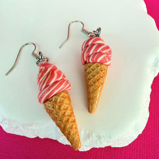 Ice cream cone dangle earrings in pink swirl design with silver toned hooks on a white stone with a pink background.