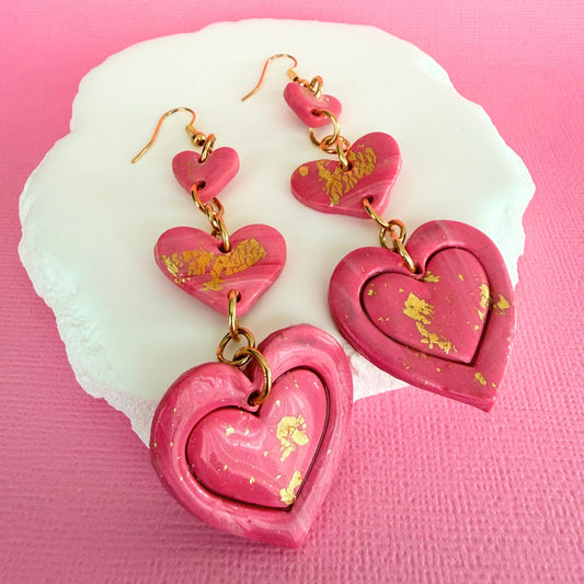 Australian handmade heart-shaped pink dangle earrings with gold accents on a pink background.