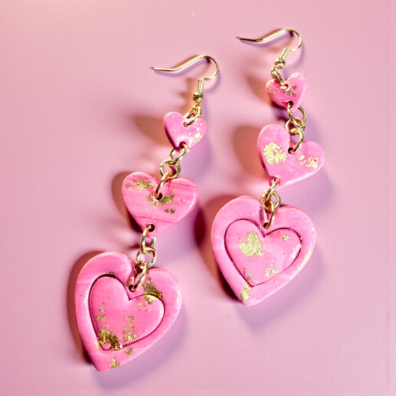 Pair of pink handmade polymer clay heart dangle earrings with gold leaf detail on a pink background