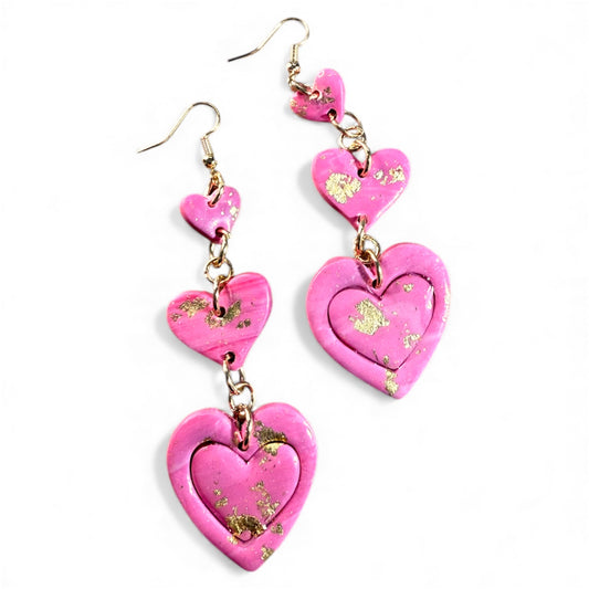 Pink heart-inspired polymer clay statement dangle earrings with gold details on a white background.