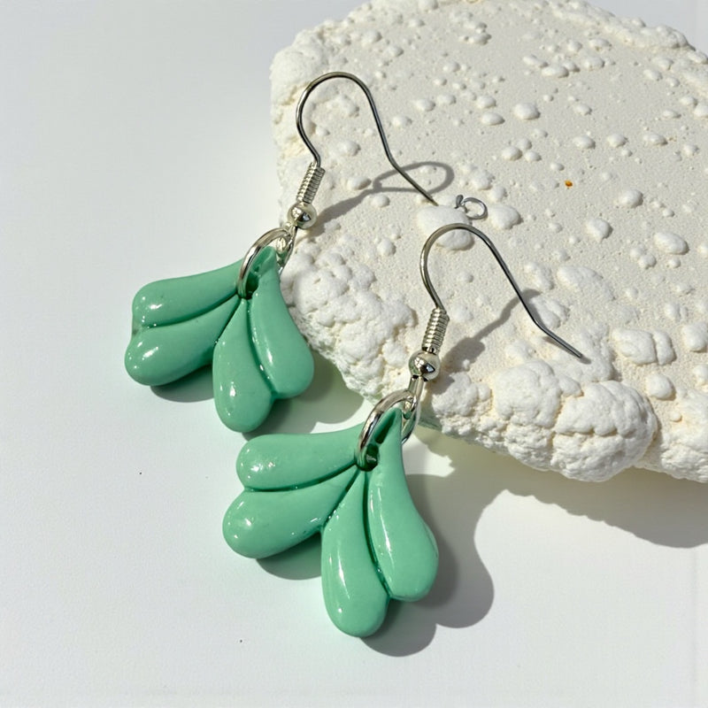 mermaid tail shaped polymer clay dangle earrings in mint green colour on a pale green background 