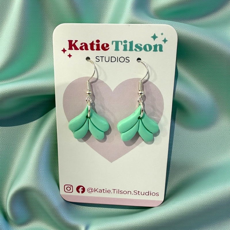 Green mermaid tail earrings on a Katie Tilson Studios card with a heart design.