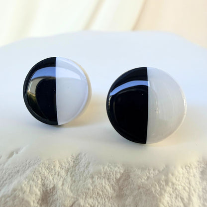 Black and white half and half circular stud earrings on a textured white surface.