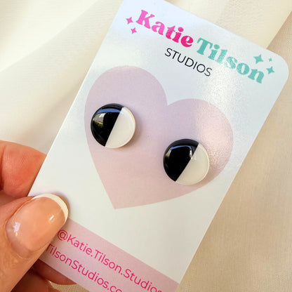 Black and white half and half circular stud earrings on a Katie Tilson Studios earring card held by a hand.
