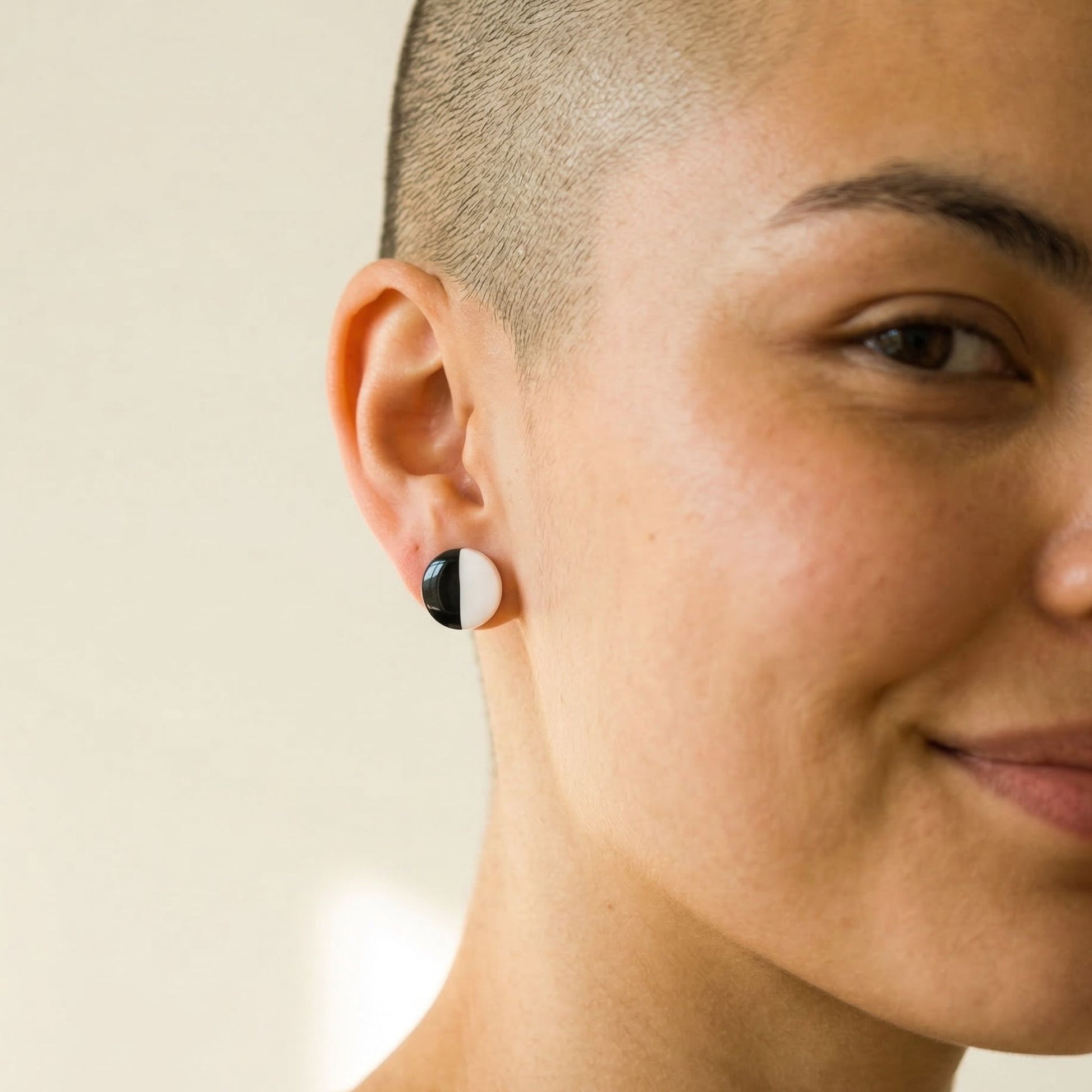 Close-up of a person wearing a black and white circular stud earring on a neutral background.
