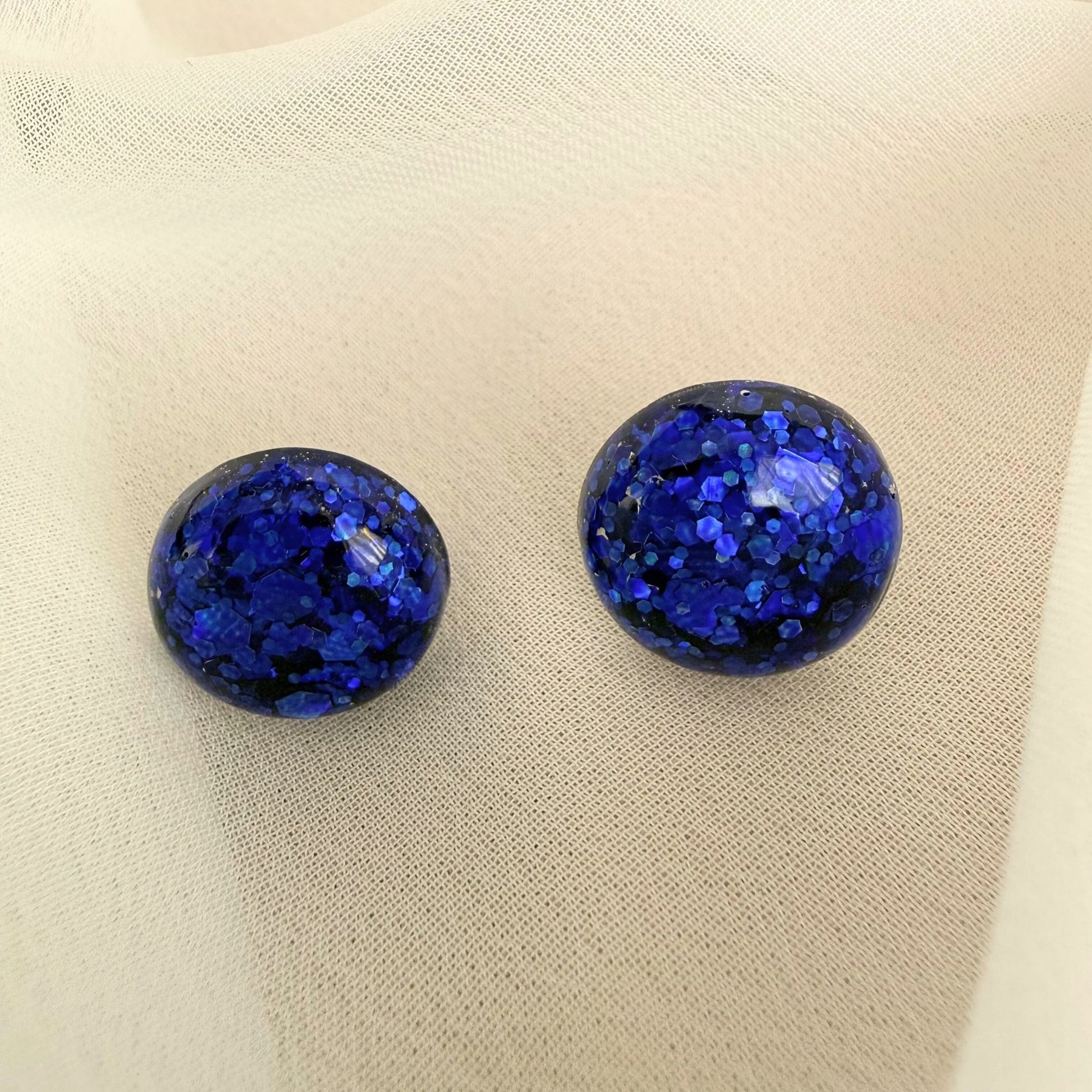 Midnight Glow blue stud earrings resting on white fabric.
