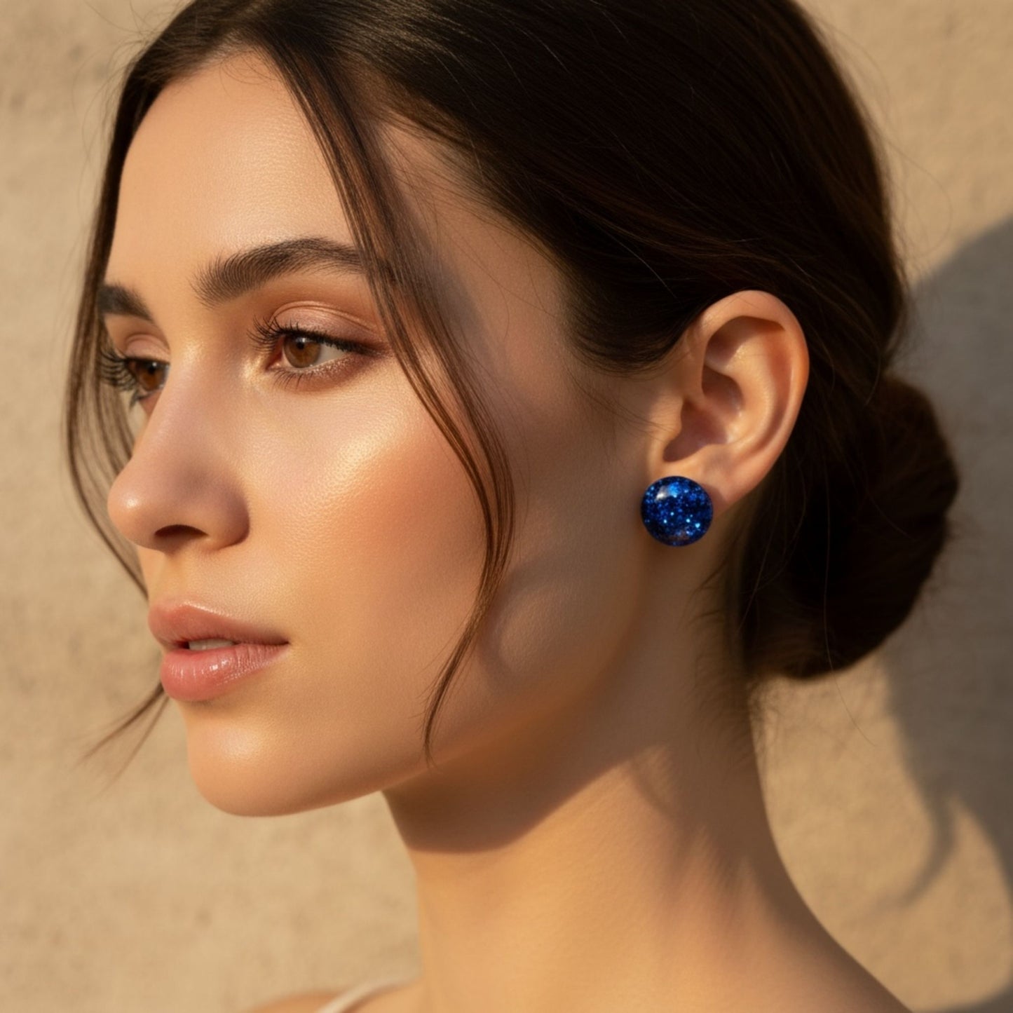 Close-up of a woman wearing Australian handmade blue resin stud earrings against a neutral background.