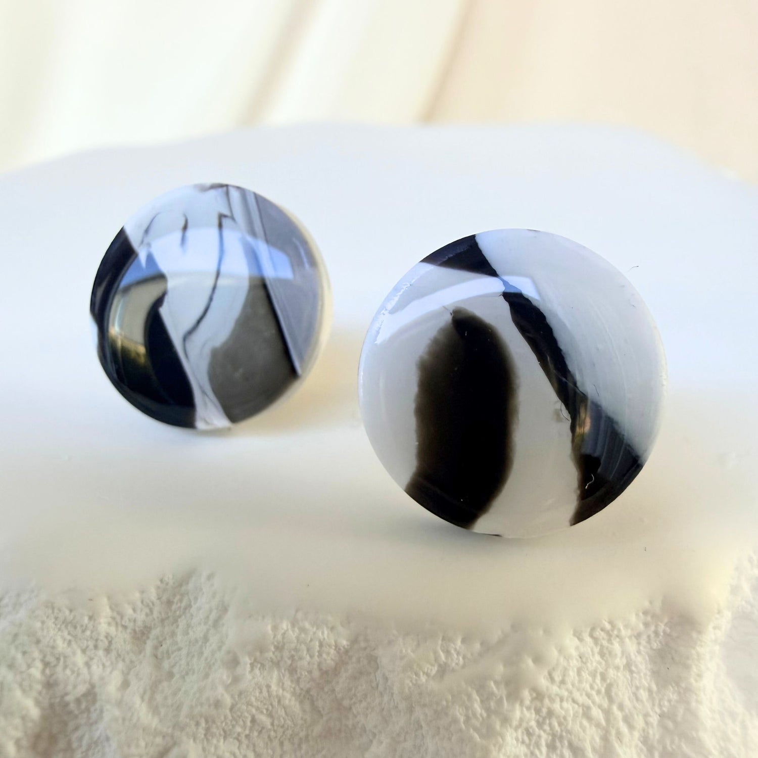 Black and white marbled round studs with a glossy finish on a white textured surface.