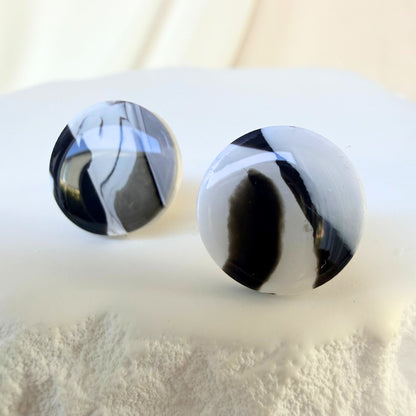 Black and white marbled round studs with a glossy finish on a white textured surface.