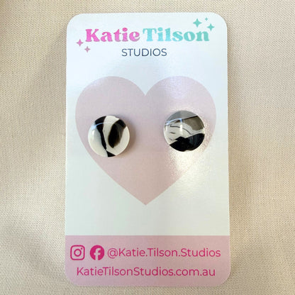 Midnight black and white marbled design circular stud earrings on a Katie Tilson Studios earring card against a beige background.