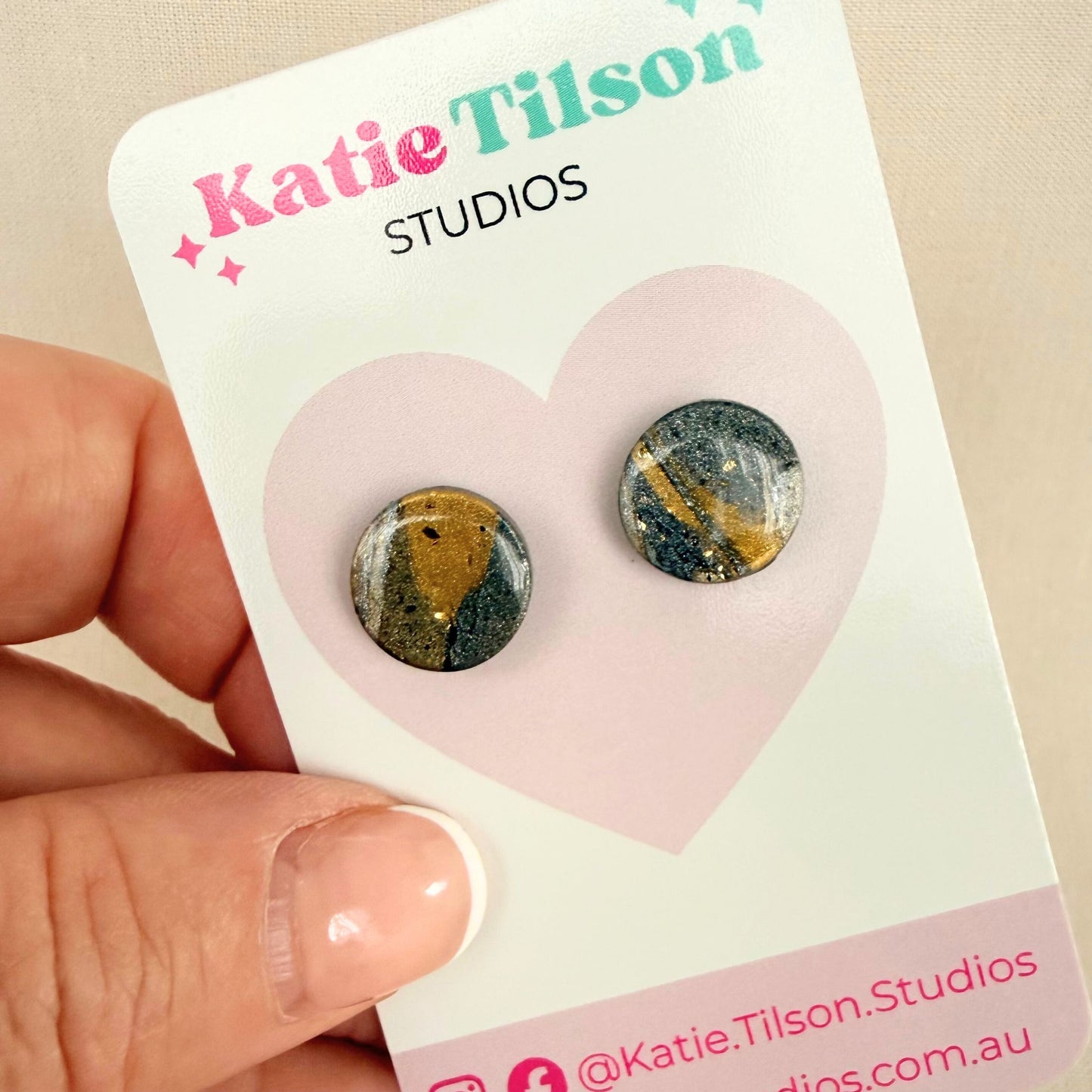 Gold and silver abstract design stud earrings on a Katie Tilson Studios card held by a hand.