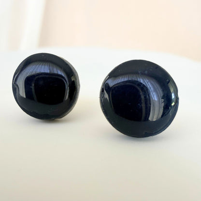 A pair of deep midnight colour circle studs with a glossy resin finish resting on a white surface.