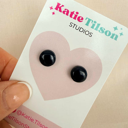 Black circular stud earrings on a Katie Tilson Studios card held by a hand.