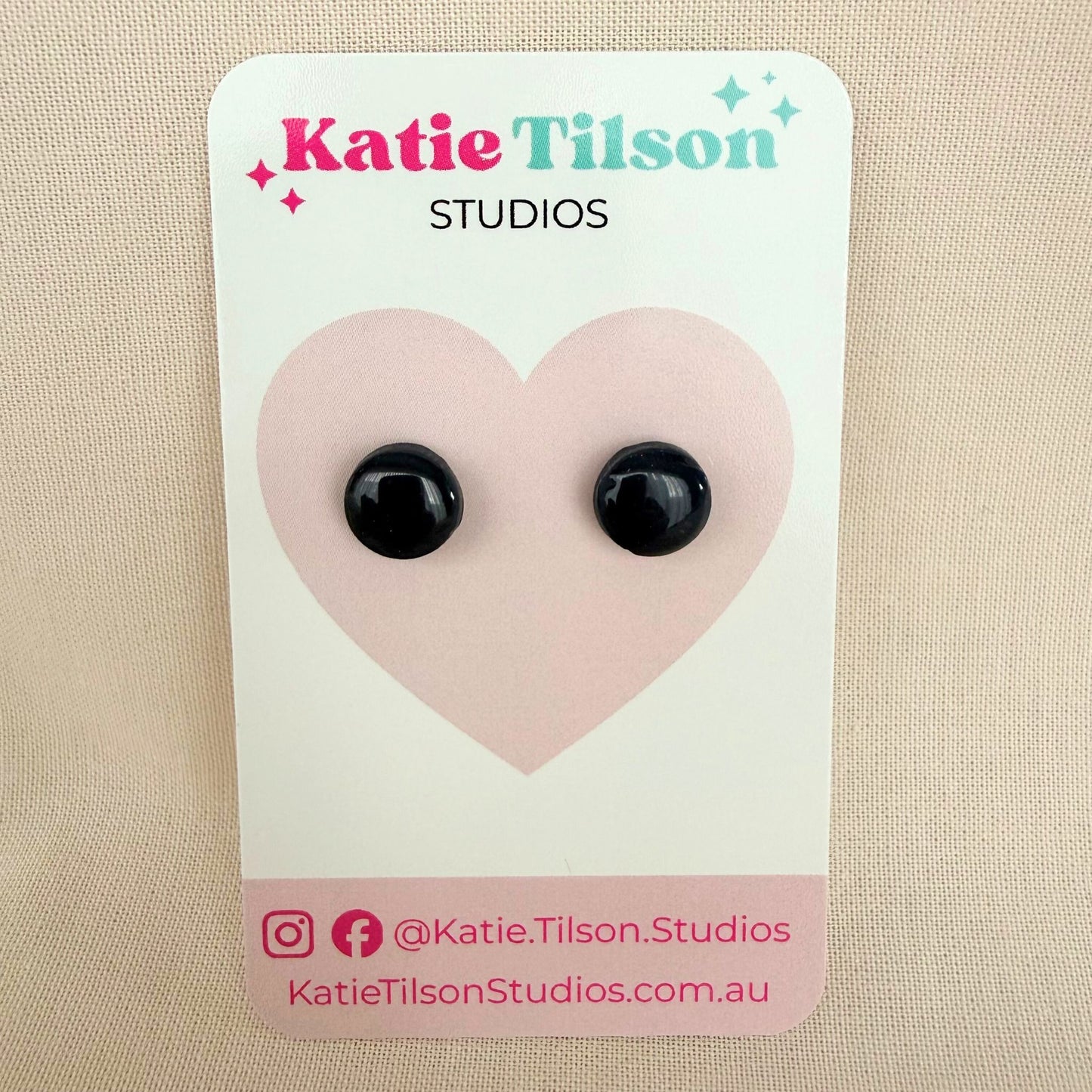 Black circular stud earrings on a Katie Tilson Studios card against a beige background.