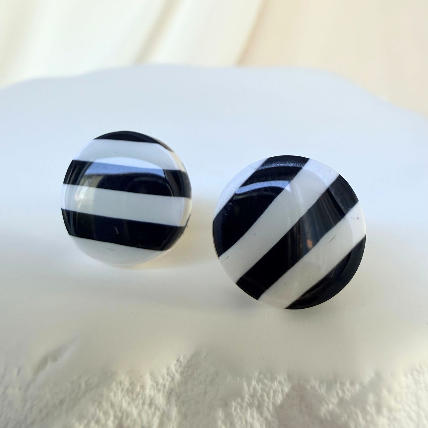 Black and white striped circular stud earrings on a white surface.