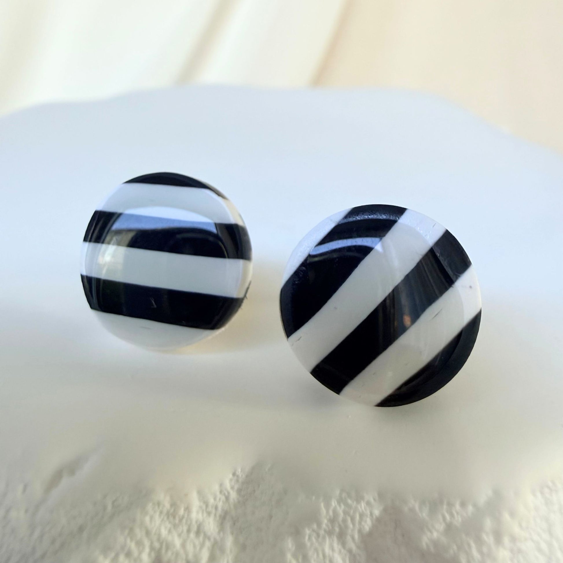Black and white striped circular stud earrings on a white surface.