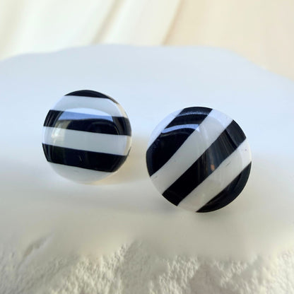 Black and white striped circular stud earrings on a white surface.