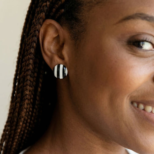 Close-up of a woman wearing black and white striped stud earrings.