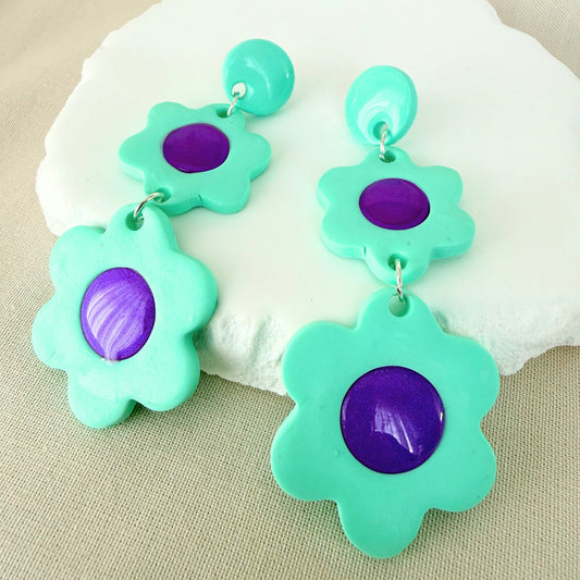Mint green flower dangle earrings with glossy violet centres on a white surface.