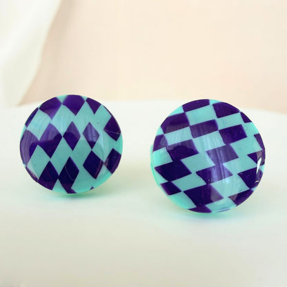 A pair of mint and purple checkered pattern circle studs with shimmer and glossy resin finish resting on a white surface.