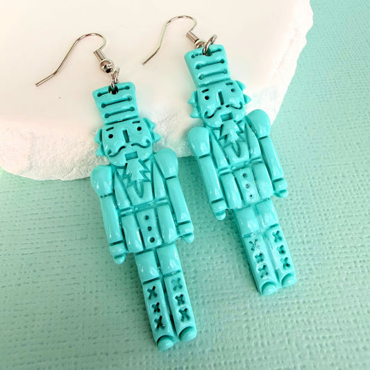 Australian handmade turquoise nutcracker-shaped dangle earrings with silver toned hooks on a light green background.
