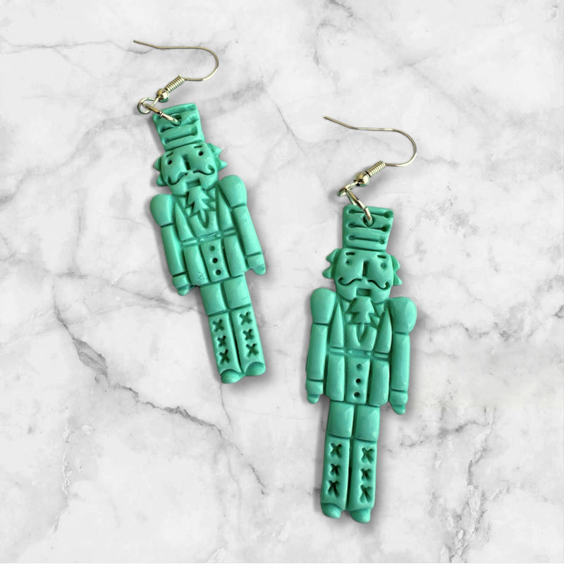 mint green nutcracker design polymer clay earrings on a marble background
