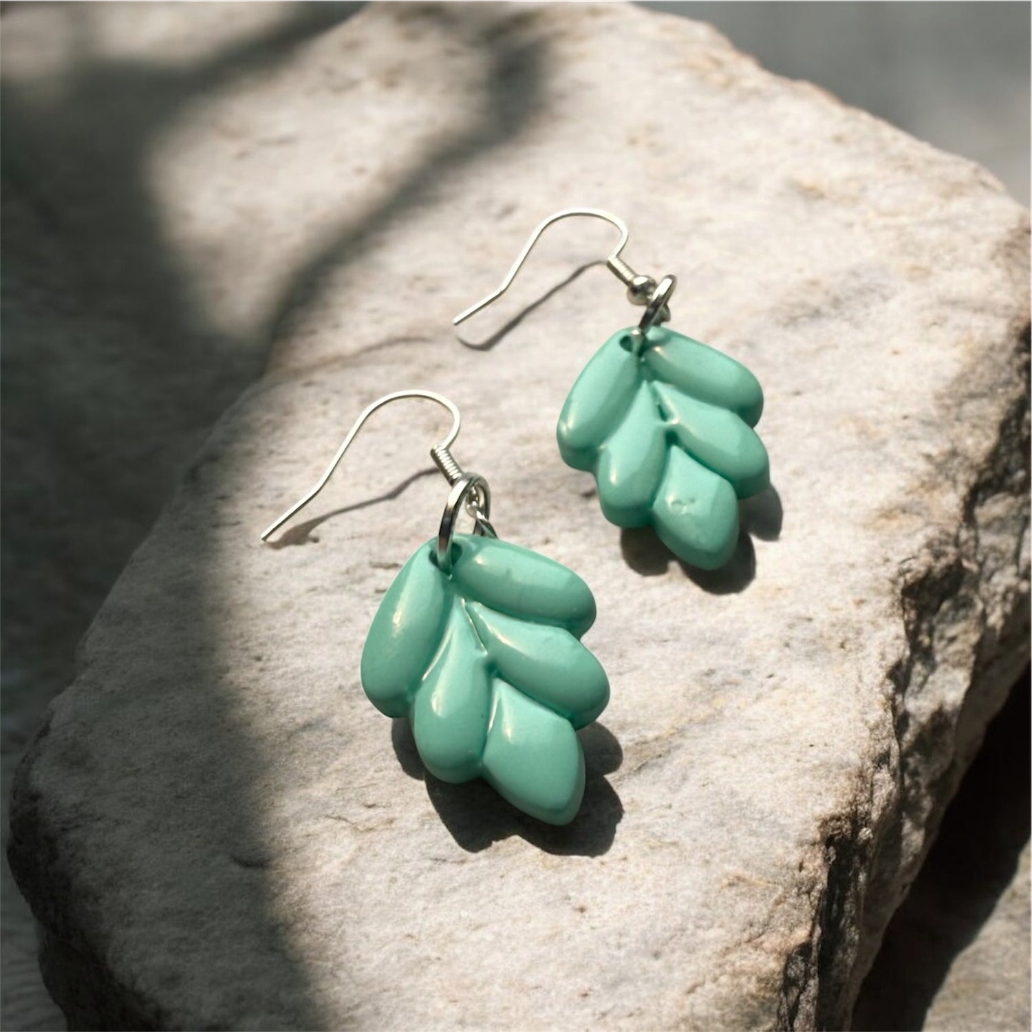 mint green leaf-shaped dangle earrings on a stone surface 