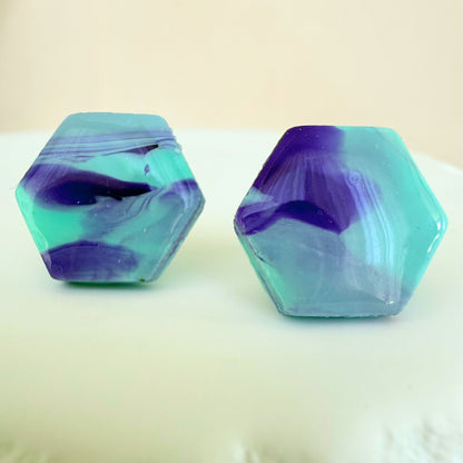 A pair of mint and violet marble hexagon shaped studs with a glossy resin finish resting on a white surface.
