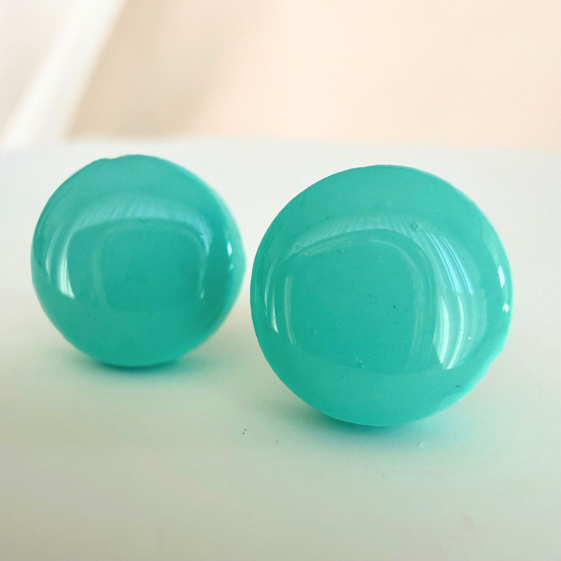 A pair of mint colour circle studs with a glossy resin finish resting on a white surface.