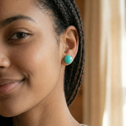 Close-up of a woman wearing round mint green stud earrings with a glossy finish against a blurred background.