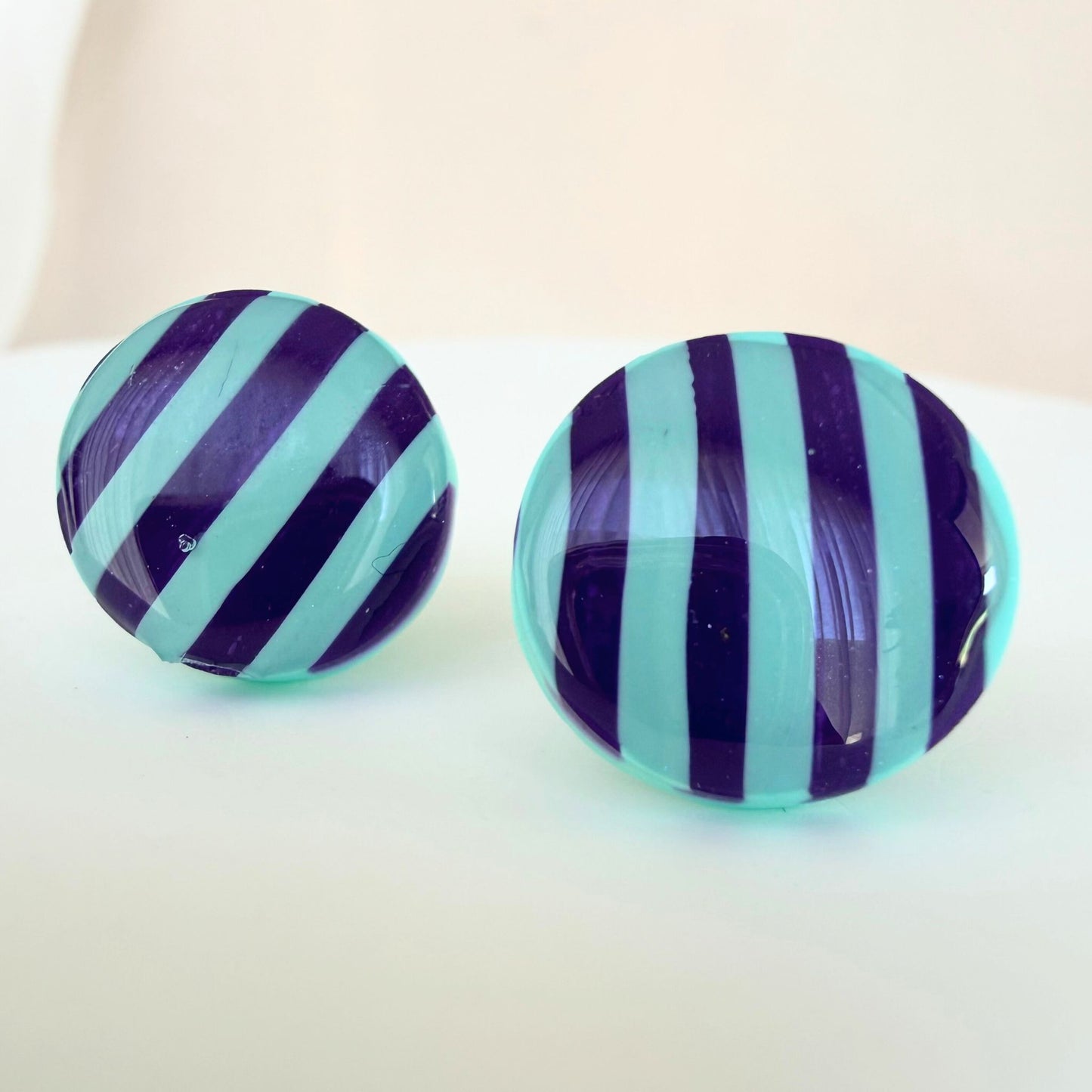A pair of bright mint and purple stripe circle studs with shimmer and glossy resin finish resting on a white surface.