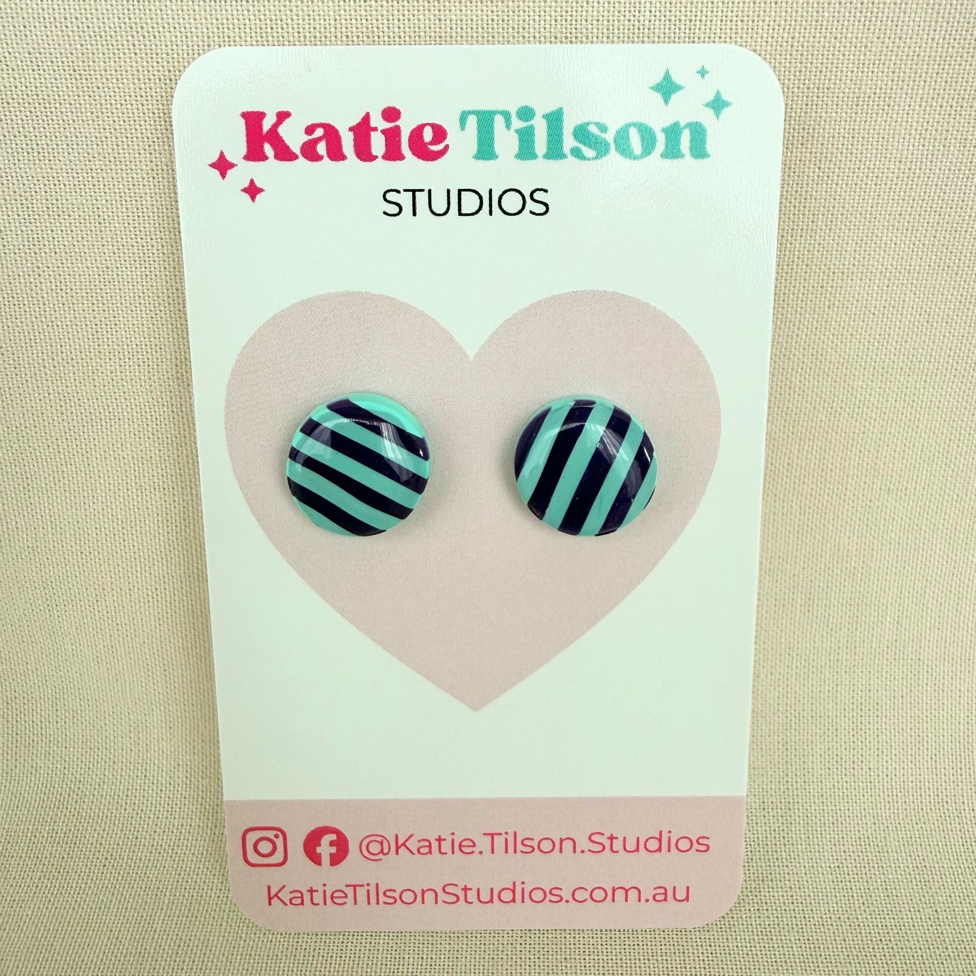 Pair of mint and violet striped round stud earrings on a Katie Tilson Studios card with a beige background.