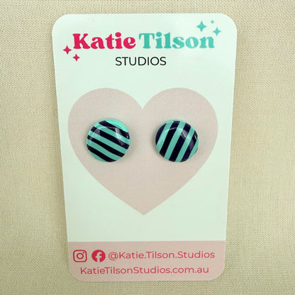 Pair of mint and violet striped round stud earrings on a Katie Tilson Studios card with a beige background.
