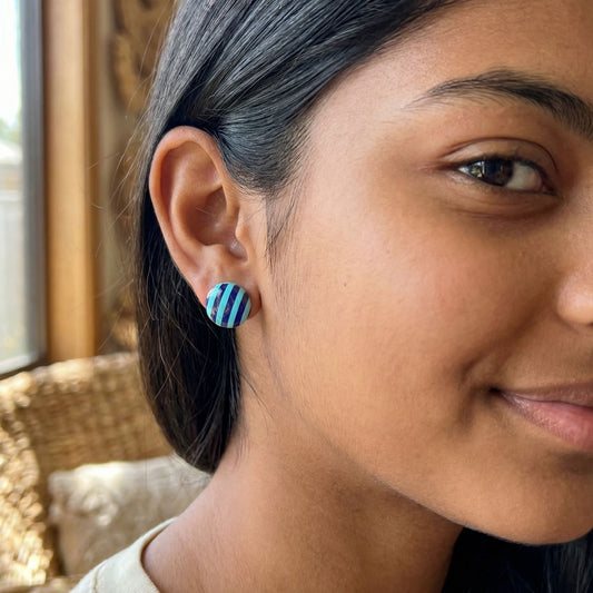 Close-up of a woman wearing mint and violet striped circular stud earrings.