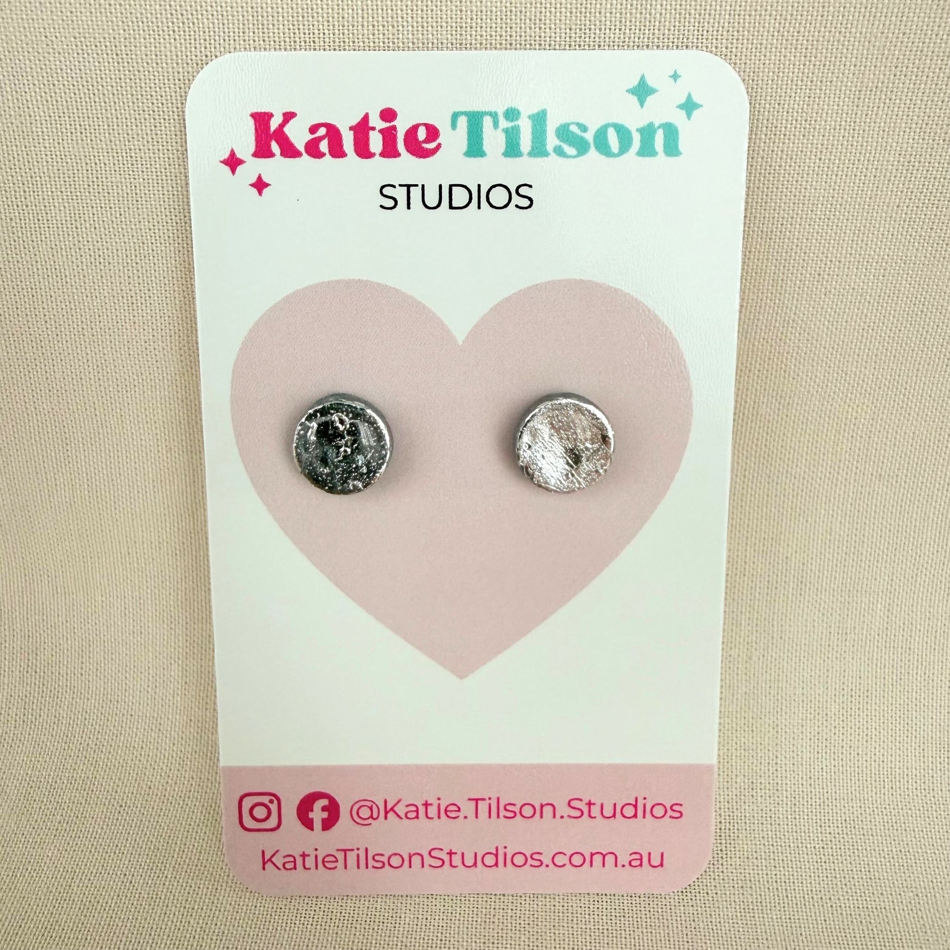 Pair of silver coloured circular stud earrings on a Katie Tilson Studios card against a beige background.