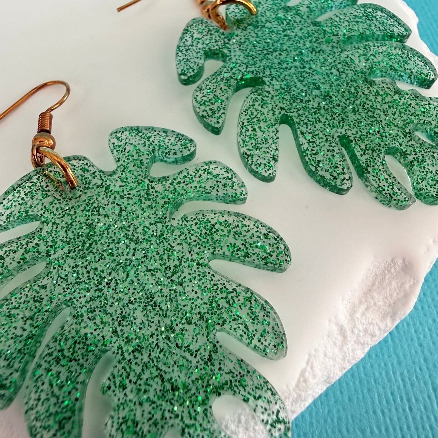 Close up of Australian handmade resin earrings Monstera Leaf in green glitter design with gold toned hardware.